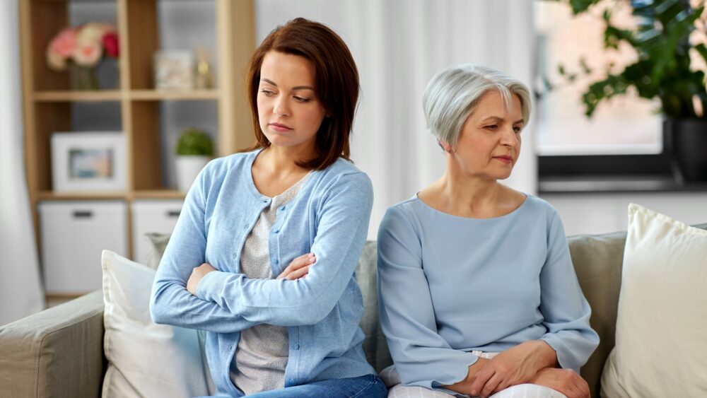 Two people sitting back-to-back on a sofa in silence, illustrating tension and conflict in inheritance dispute